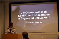 Eine Frau in Uniform hält einen Vortrag über die Ostsee; auf der Leinwand steht: 'Die Ostsee zwischen Konflikt und Kooperation'.