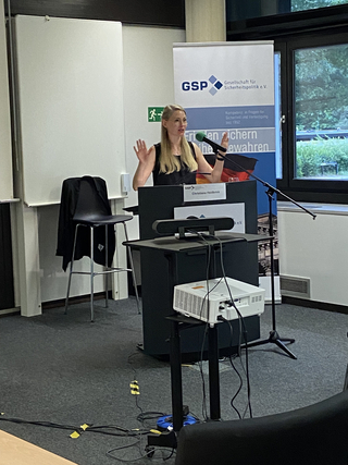 Christiane Heidbrink spricht auf einer GSP-Veranstaltung, gestikuliert vor einem Rednerpult und Banner.