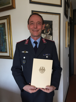 Lächelnder Mann in deutscher Militäruniform, Lobert, hält ein Dokument mit dem Bundesadler.