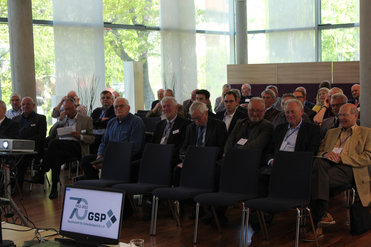 Publikum einer GSP-Konferenz, die das 70-jährige Jubiläum feiert, mit dem Logo auf einem Laptop-Bildschirm.