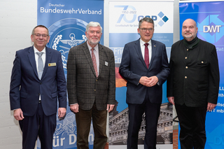 Vier Männer, darunter Harald Lem, in unterschiedlicher Kleidung (Anzüge, gemusterte Jacke, Janker) posieren bei einem Sicherheitsevent.