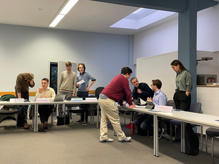 Studenten nehmen an einer Model United Nations (MUN)-Simulation teil und diskutieren an Tischen mit Ländernamensschildern.