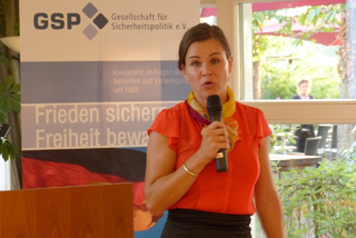 Eine Frau spricht in ein Mikrofon vor einem Banner der Gesellschaft für Sicherheitspolitik (GSP).