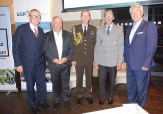 Fünf Männer, zwei in Militäruniformen und drei in Anzügen, stehen bei einer formellen Veranstaltung.