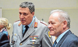 Ein Militäroffizier in grauer Uniform mit Orden spricht mit einem älteren Mann im blauen Anzug bei einer Veranstaltung.
