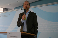Tobias Pietz spricht am Rednerpult mit Mikrofon vor dem Logo des Presse- und Informationsamts der Bundesregierung.