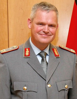 Lächelnder Militäroffizier in grauer Uniform mit goldenen Abzeichen.