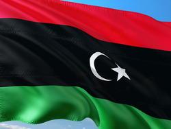 Die Flagge Libyens: rot, schwarz, grün gestreift, mit weißem Halbmond und Stern auf dem schwarzen Streifen, wehend vor blauem Himmel.