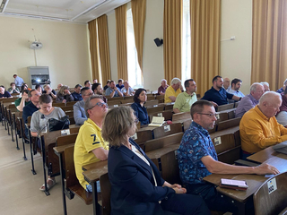 Eine Gruppe von Erwachsenen sitzt in Reihen in einem Hörsaal und lauscht einer Präsentation oder Diskussion.