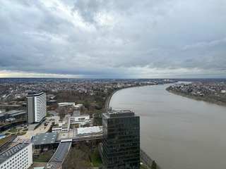 Erhöhte Ansicht einer Stadt mit einem breiten Fluss, modernen Gebäuden und einem bewölkten Himmel.