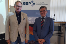 Zwei Männer stehen lächelnd vor einem Banner der Gesellschaft für Sicherheitspolitik e.V.