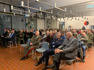 Eine Gruppe von Menschen, viele in Militäruniformen, sitzt in einem großen Raum während einer Veranstaltung oder Präsentation.