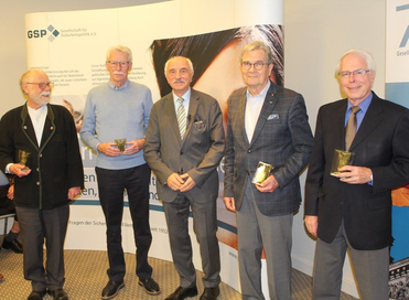 Fünf Männer lächeln, halten goldene Auszeichnungen in den Händen und stehen vor einem Banner der GSP Sicherheitspolitik.