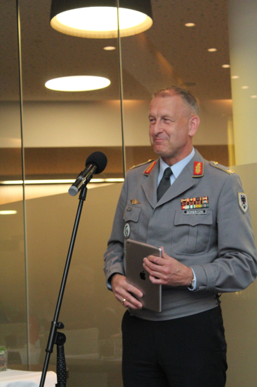 Lächelnder deutscher Militäroffizier Sembritzki in Uniform, ein Tablet haltend, neben einem Mikrofon.