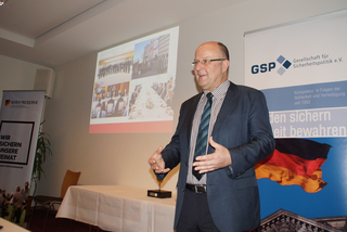 Mann präsentiert bei Veranstaltung mit Projektion von Gruppenbildern und Bannern der Gesellschaft für Sicherheitspolitik und Wir sind die Reserve.