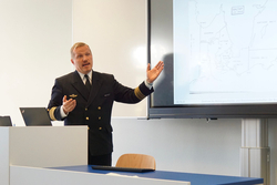 Ein Marineoffizier in Uniform präsentiert eine Karte der Ostseegebiete auf einem Bildschirm und gestikuliert dabei.