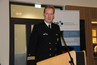 Marineoffizier in Uniform spricht am Rednerpult vor einem Banner der Gesellschaft für Sicherheitspolitik e.V.