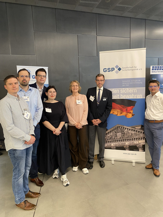 Sieben Personen posieren vor einem Banner der Gesellschaft für Sicherheitspolitik (GSP) mit dem Reichstagsgebäude.