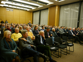 Ein großes Publikum, hauptsächlich Männer, in Reihen sitzend in einem Konferenzraum, bei einem Vortrag.