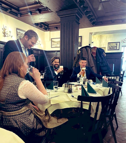 Gruppe von Menschen in einem traditionellen Restaurant, einer spricht ins Mikrofon, andere trinken Bier und lachen.