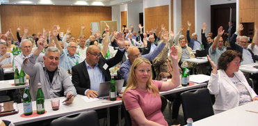 Publikum in einem Konferenzraum hebt die Hände zur Abstimmung oder Zustimmung.