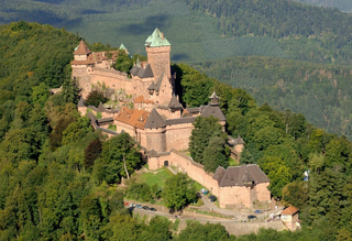 Hochkönigsburg, mittelalterliche Festung mit roten Steinmauern und grünen Dächern, umgeben von dichtem Wald auf einem Hügel.