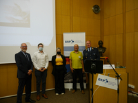 Fünf Personen, darunter eine Frau und ein Mann in Uniform, lächeln bei einer sicherheitspolitischen Veranstaltung vor einem Banner.