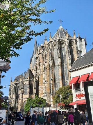 Der Aachener Dom, eine prächtige gotische Kirche, ragt unter blauem Himmel empor, mit Menschen im Vordergrund.