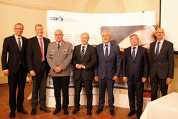 Sieben Männer in Anzügen und einer in Militäruniform posieren vor einem Banner der GSP.