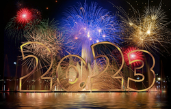 Goldene '2023'-Zahlen spiegeln sich im Wasser, darüber explodieren bunte Feuerwerke am dunklen Nachthimmel.