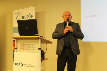 Ein Mann hält einen Vortrag bei einer GSP-Veranstaltung, mit dem GSP-Logo und 'Zielsetzung' auf einer Leinwand.