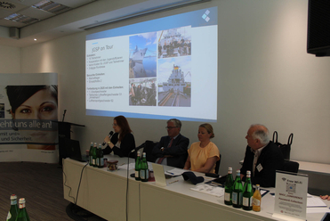 Konferenzraum mit vier Rednern an einem Tisch, dahinter eine Präsentation zu 'JGSP on Tour' mit Bildern von Schiffen.