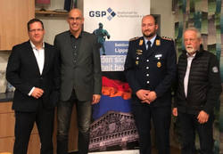 Vier Männer, darunter einer in Uniform, stehen vor einem Banner der Gesellschaft für Sicherheitspolitik.