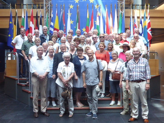 Große Gruppe von Erwachsenen posiert vor der EU-Flagge und nationalen Flaggen europäischer Länder.