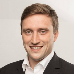 Porträt eines lächelnden Mannes mit kurzen braunen Haaren, Anzug und weißem Hemd.