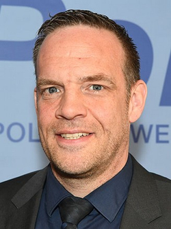 Stefan Raab, ein deutscher Fernsehmoderator, lächelt, trägt einen dunklen Anzug mit Hemd und Krawatte.