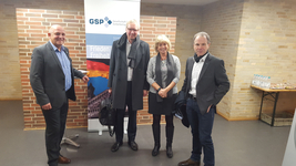 Vier Personen lächeln und posieren vor einem GSP-Banner mit den deutschen Flaggenfarben und dem Brandenburger Tor.