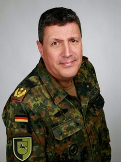 Ein lächelnder deutscher Offizier in Flecktarn-Uniform mit Dienstgradabzeichen und Einheitsabzeichen.