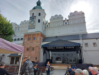 Ein historisches Schloss in Stettin mit Uhrturm, einer aufgebauten Bühne und Publikum, das einer Rednerin zuhört.
