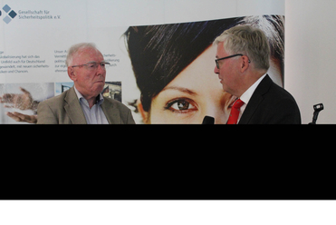 Zwei Männer in Diskussion bei einer Veranstaltung der Gesellschaft für Sicherheitspolitik, einer spricht ins Mikrofon.