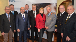 Eine Gruppe von neun Personen, die meisten Männer, in Anzügen und Uniformen vor einem Banner der Gesellschaft für Sicherheitspolitik.