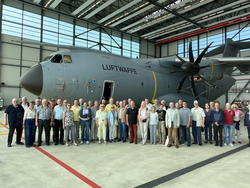 Große Gruppe von Besuchern posiert vor einem Transportflugzeug A400M Atlas der Luftwaffe in einem Hangar.