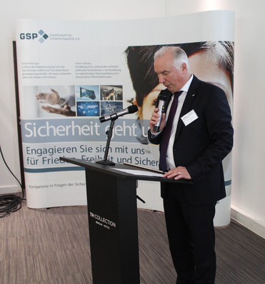 Mann im Anzug spricht am Rednerpult mit Mikrofon vor einem Banner der 'GSP Gesellschaft für Sicherheitspolitik e.V.'.