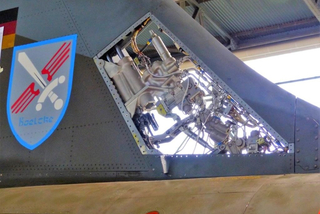 Blick in das Innere eines Militärjets: geöffnete Klappe am Heck mit freigelegten Hydraulikleitungen, Stellgliedern und "Boelcke"-Wappen.