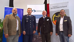 Vier Männer, darunter einer in Uniform, stehen vor Bannern der Gesellschaft für Sicherheitspolitik und des Deutschen BundeswehrVerbandes.